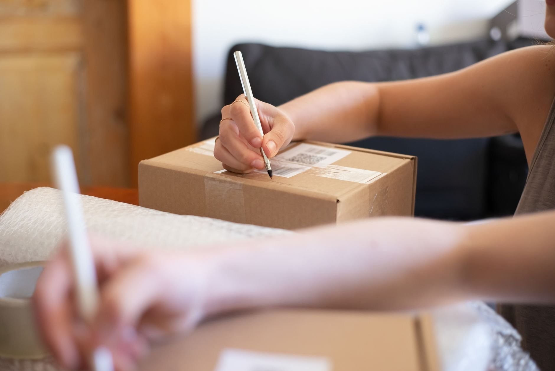 Hands labeling a cardboard shipping box for online orders from a home office.